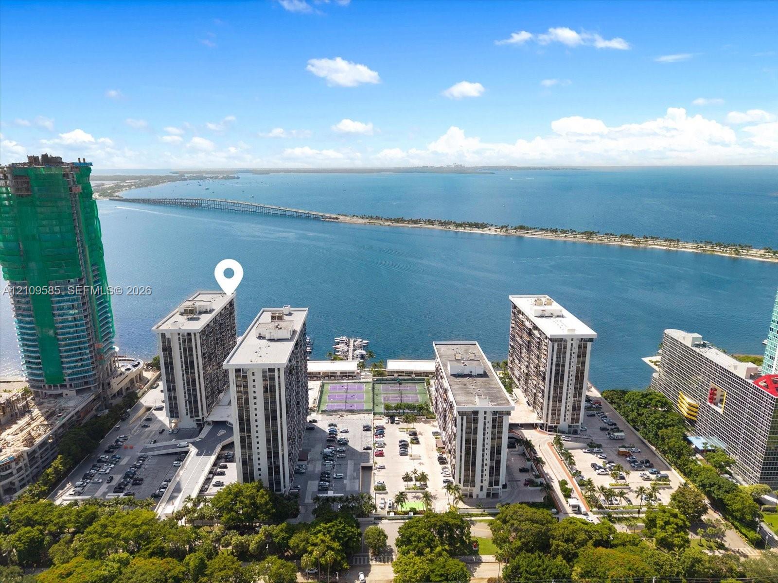 Waterfront high-rise complex featuring multiple tennis courts, a private dock, and expansive surface parking