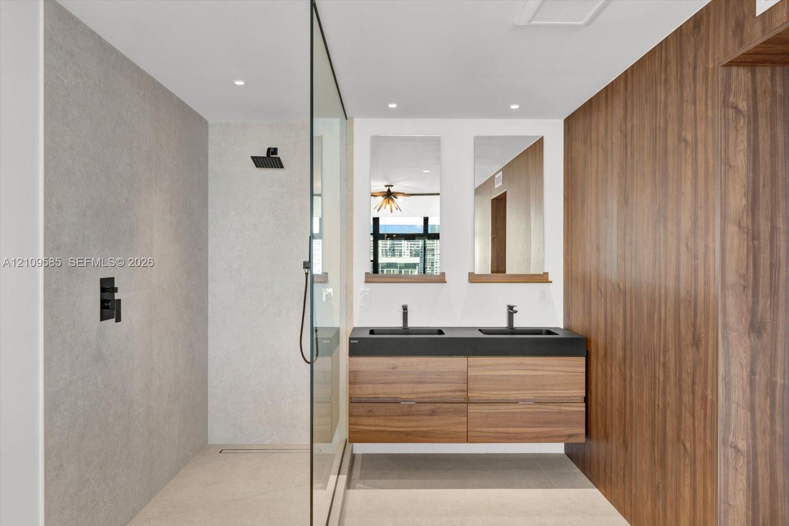 Floating wood-finish double vanity with matte black fixtures, stone-style shower surround, glass shower enclosure, and wood-finish accent wall