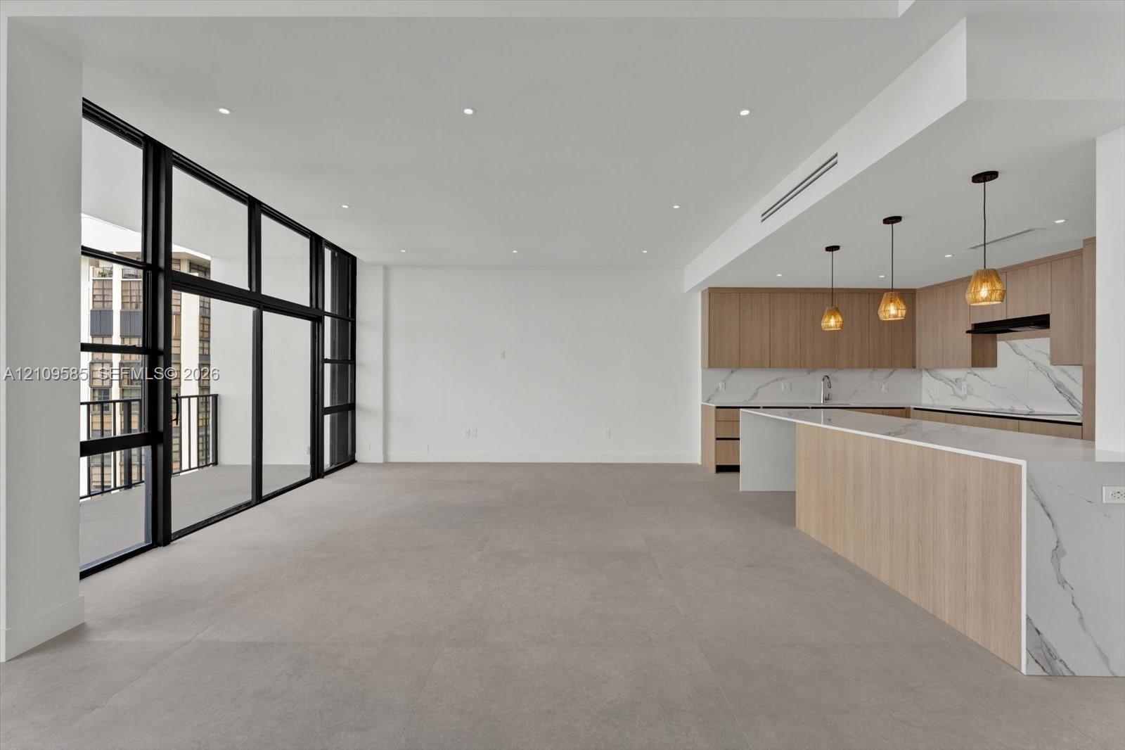 Open-concept interior featuring floor-to-ceiling black-framed glass panels, custom wood-finish cabinetry, waterfall-edge stone countertop, stone slab backsplash, and recessed lighting