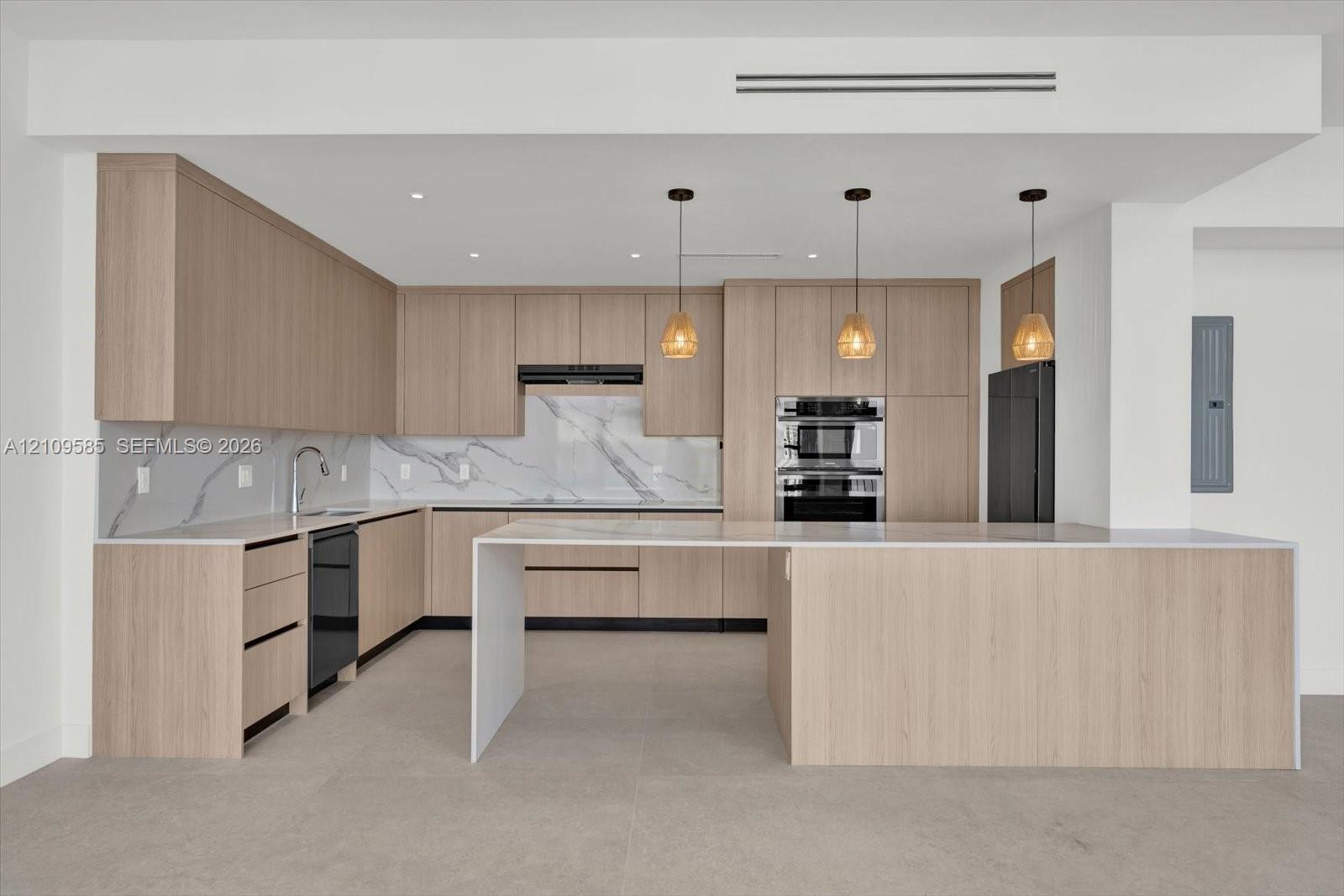 Kitchen featuring light wood-finish cabinetry, waterfall-edge island, stone-patterned backsplash, built-in double oven, and pendant lighting
