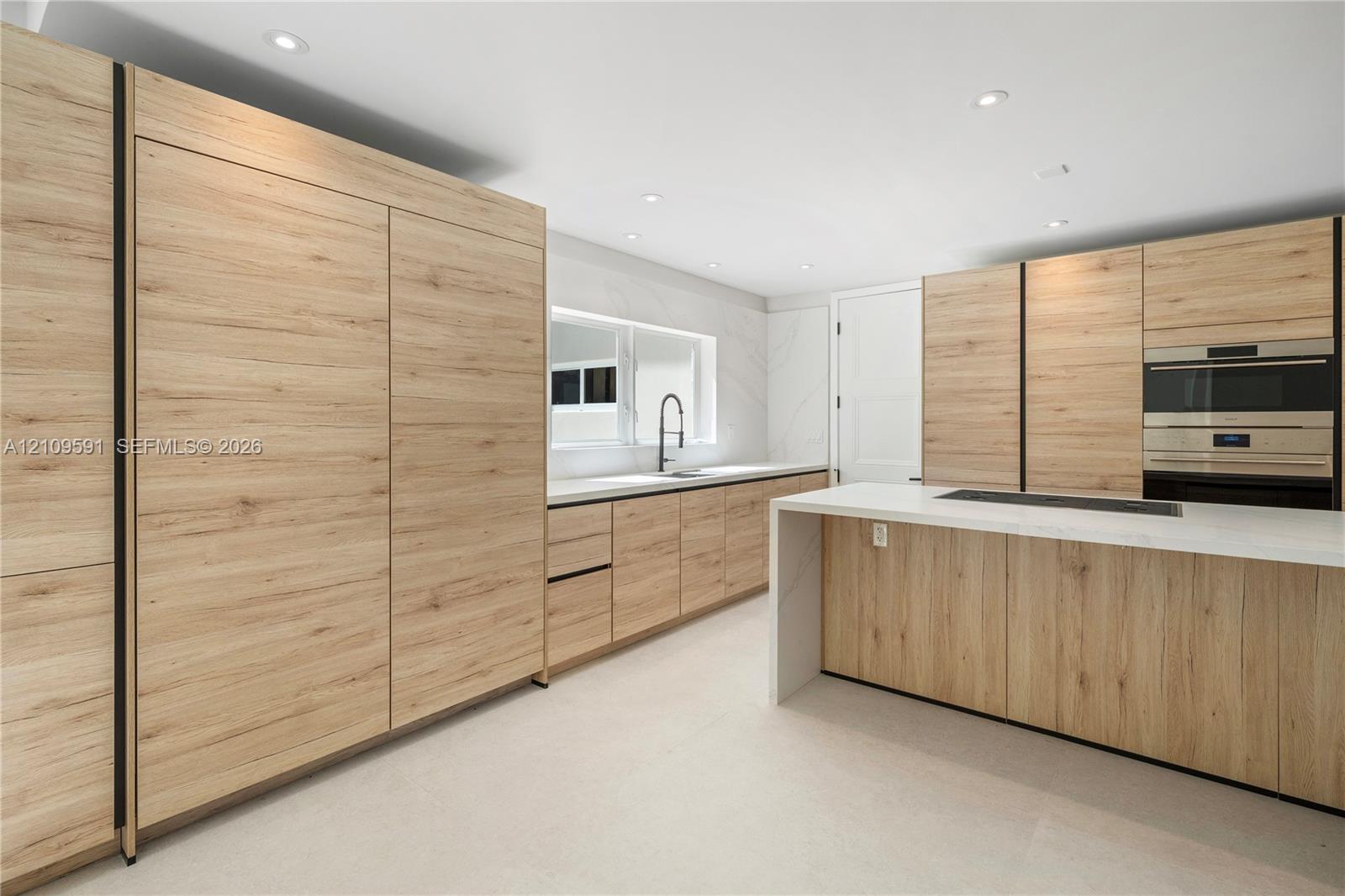 Kitchen featuring wood-finish cabinetry, a waterfall-edge island with countertop, recessed lighting, a built-in wall oven, and a single-basin sink with a matte black faucet