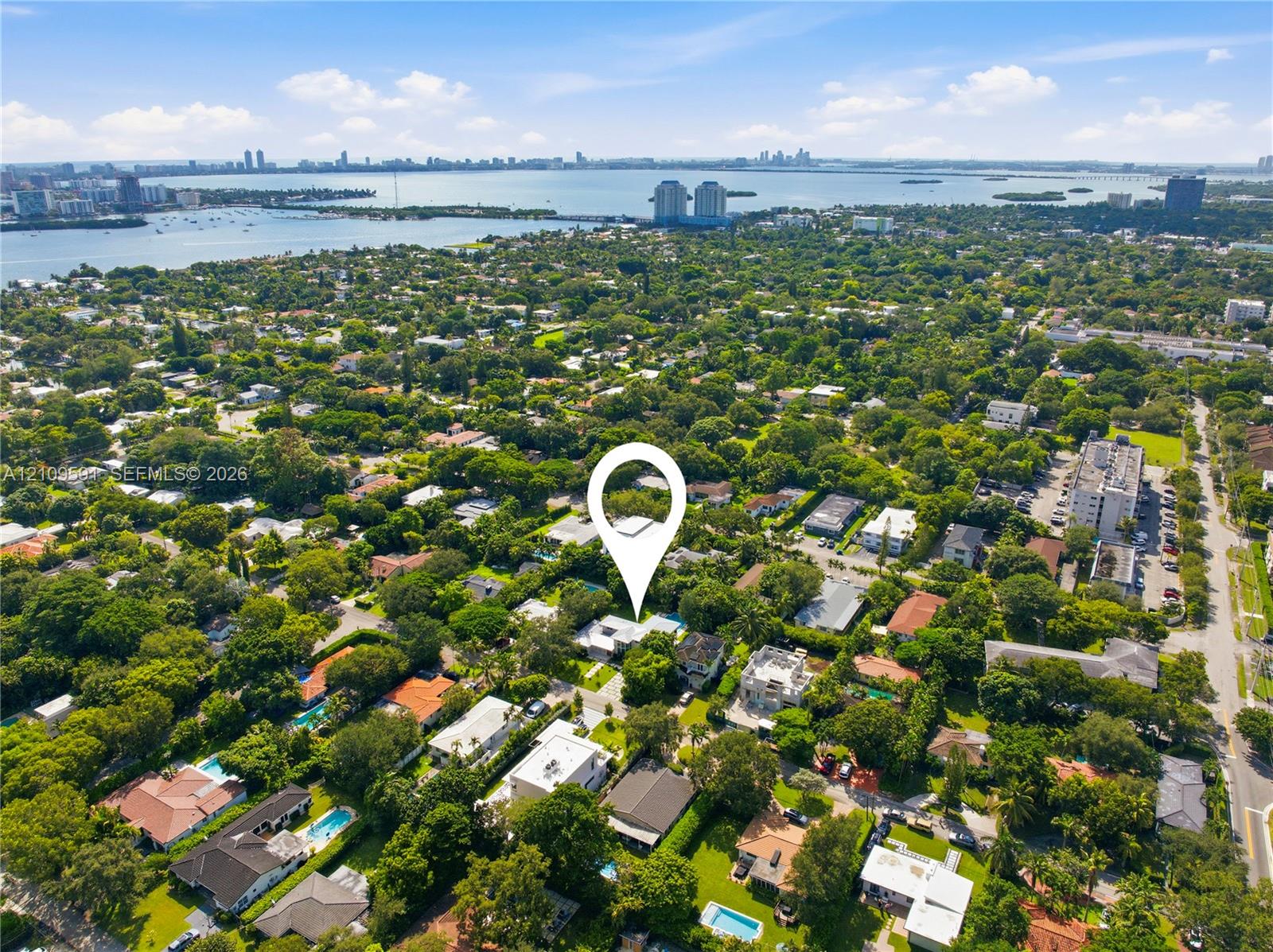 Aerial perspective of a residential lot situated within a heavily forested landscape featuring proximity to coastal waterways and an urban skyline