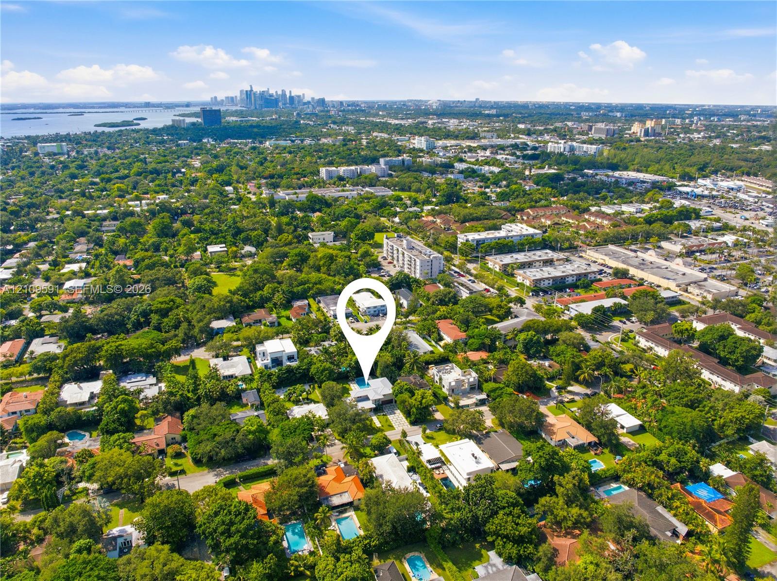 Aerial perspective of a residential property featuring a private swimming pool, mature tree canopy, and proximity to metropolitan skyline and coastal waters