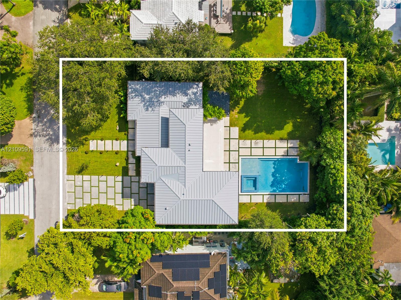 Aerial view of residential property featuring a metal roof, swimming pool with integrated spa, concrete paver hardscaping, and mature landscaping