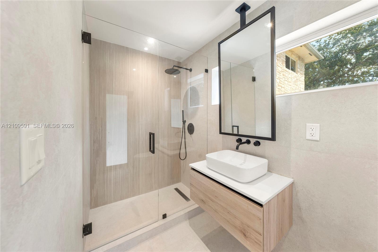 Cabana Bath Floating vanity with rectangular vessel sink and countertop, ceiling-mounted mirror with black frame, walk-in shower with frameless glass enclosure, and matte black plumbing fixtures