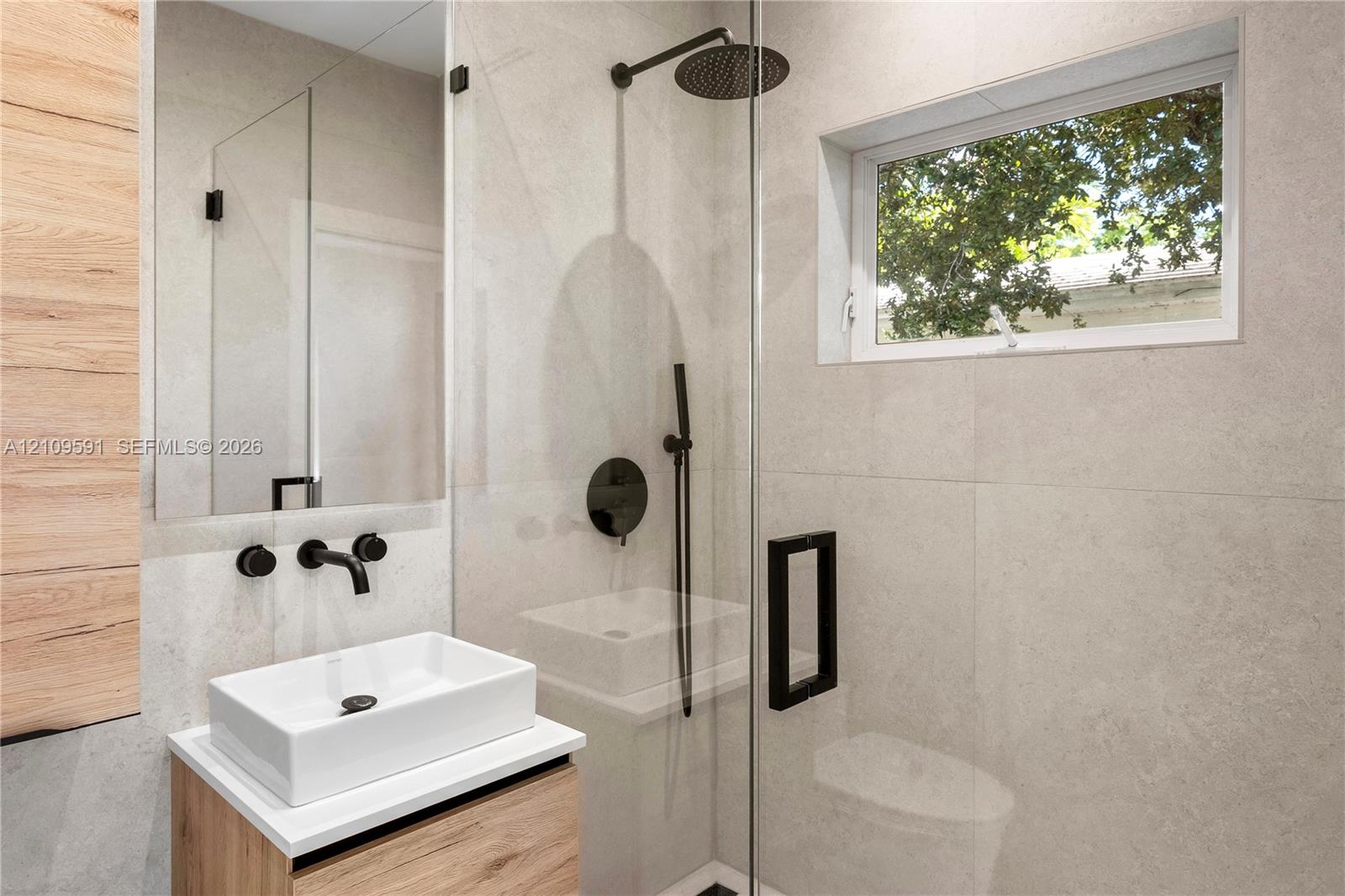 Modern bathroom featuring large-format stone-finish wall tiles, a glass-enclosed shower with matte black rainfall hardware, a wood-finish floating vanity, and a rectangular vessel sink