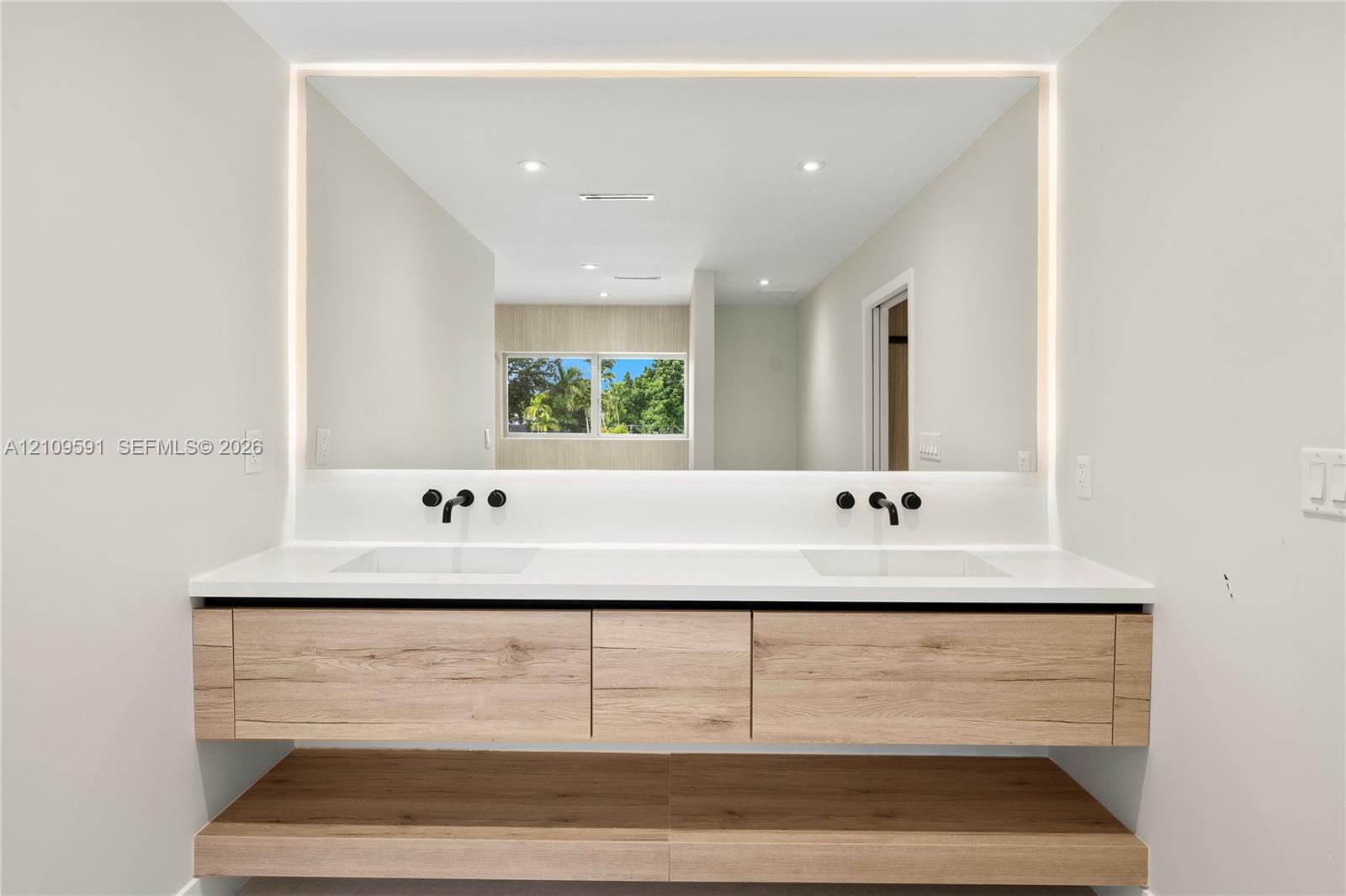Floating wood-finish vanity with dual integrated sinks, white quartz countertop, matte black wall-mounted faucets, and large LED-backlit mirror