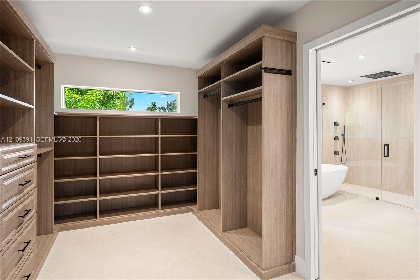 Walk-in closet featuring floor-to-ceiling wood-finish cabinetry, built-in shelving, drawers with matte black hardware, and an elongated horizontal window