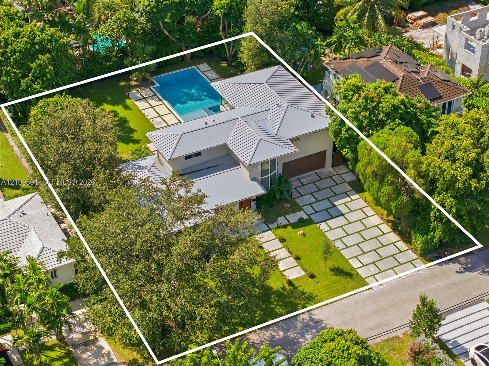 Metal roof residence featuring a swimming pool, paved hardscaping, multi-car garage, and established landscaping