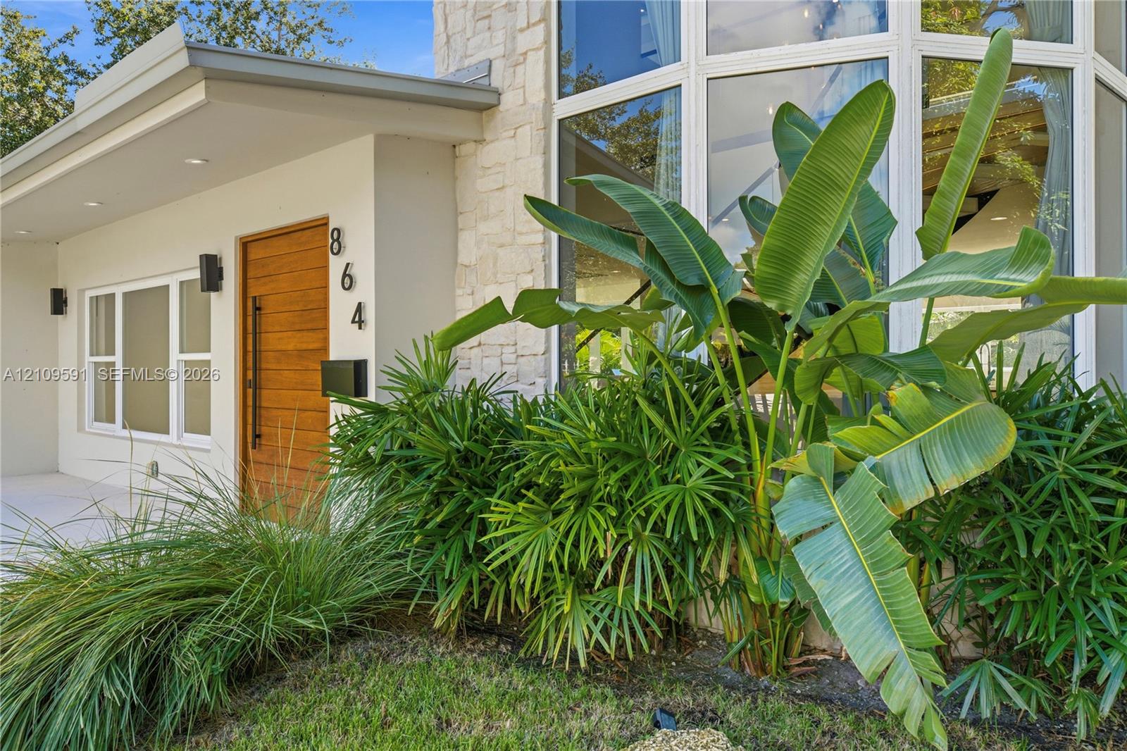 Modern facade featuring a natural stone accent wall, expansive multi-pane windows, and a horizontal wood-grain door with a vertical matte black pull handle