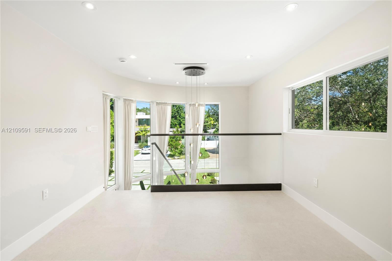 Open-concept landing featuring recessed lighting, a multi-pendant light fixture, glass railings with dark-finished metal handrails, and expansive windows