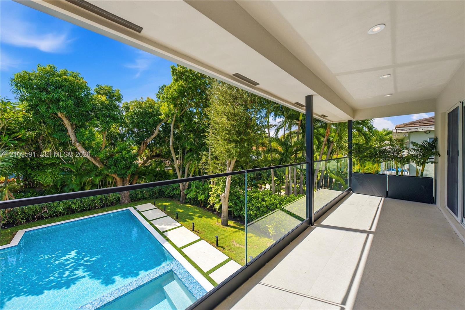 Covered balcony featuring a frameless glass railing, recessed ceiling lighting, swimming pool with integrated spa, concrete paver path, and mature landscape