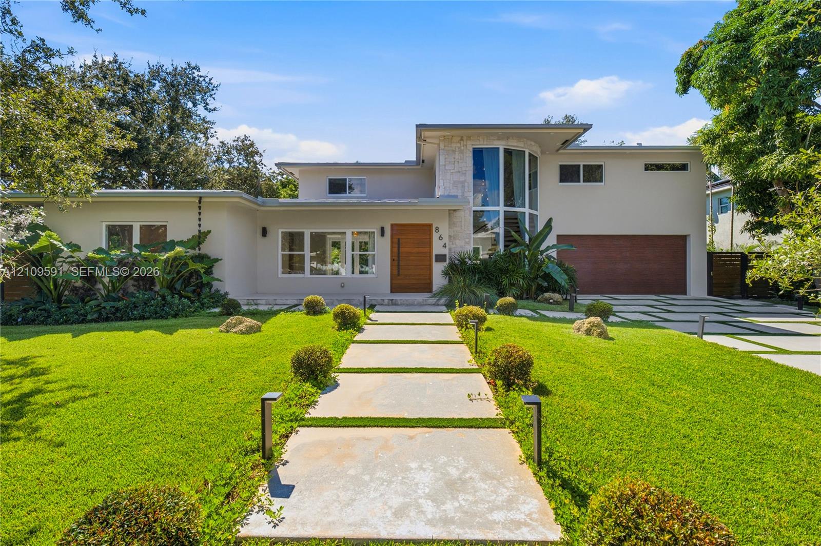 Modern exterior featuring a prominent two-story glass tower, custom horizontal wood-paneled entry door, geometric concrete paver walkway, and stone accent siding Modern exterior featuring a prominent two-story glass tower, custom horizontal wood-paneled entry door, geometric concrete paver walkway, and stone accent siding