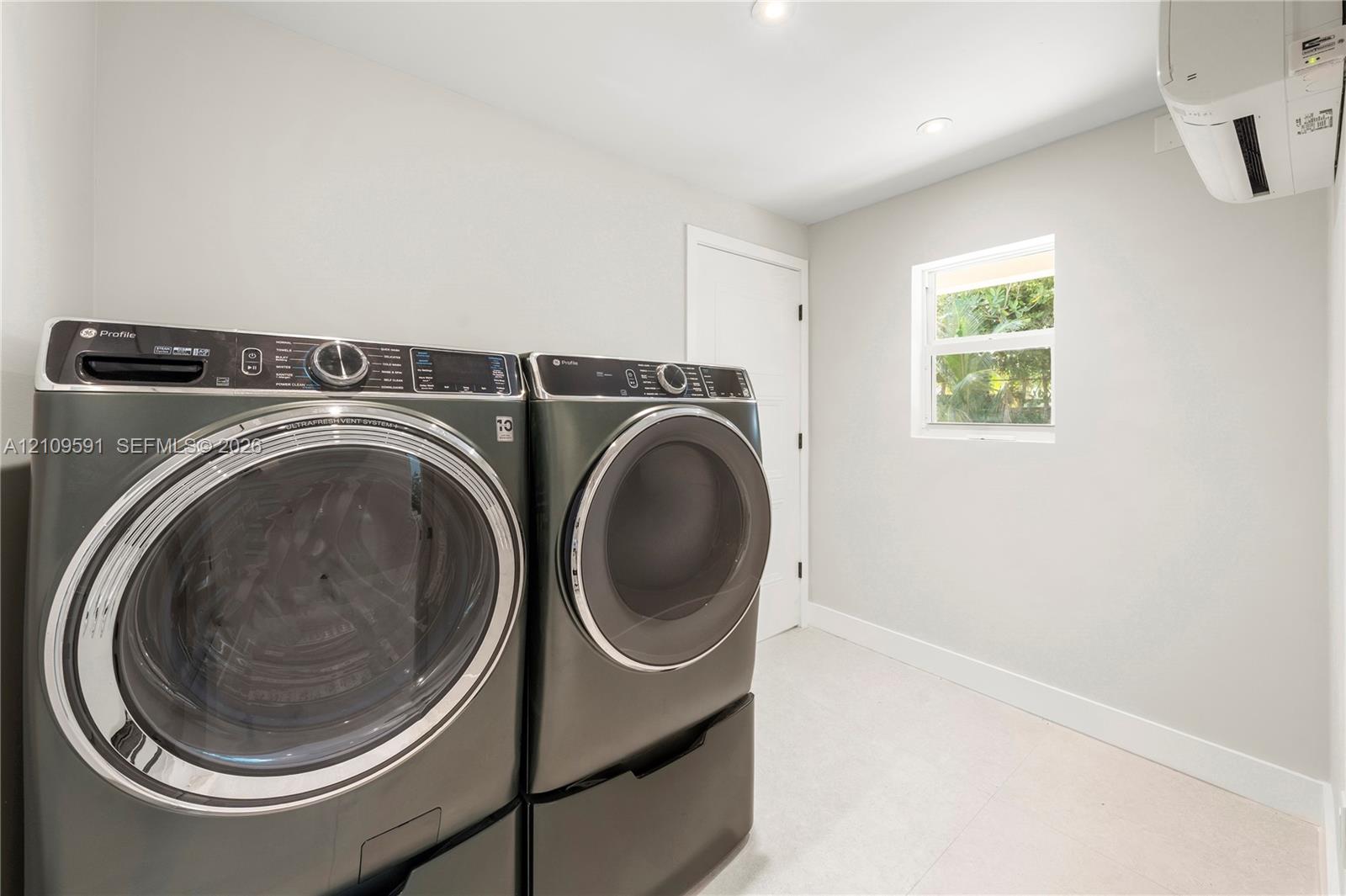 Laundry space featuring wall-mounted ductless climate control, recessed ceiling lighting, a window, and neutral-toned flooring