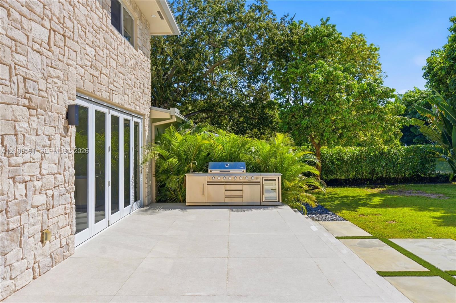 Outdoor terrace featuring a stacked stone exterior, large-format stone pavers, and a built-in stainless steel kitchen with a grill and integrated refrigeration