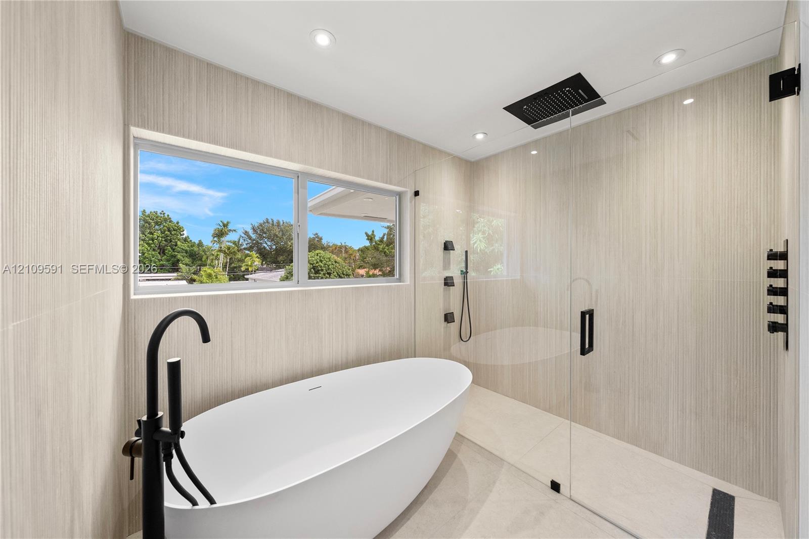 Freestanding soaking tub with matte black floor-mounted faucet, walk-in shower with frameless glass enclosure, rainfall showerhead, and neutral wall tile