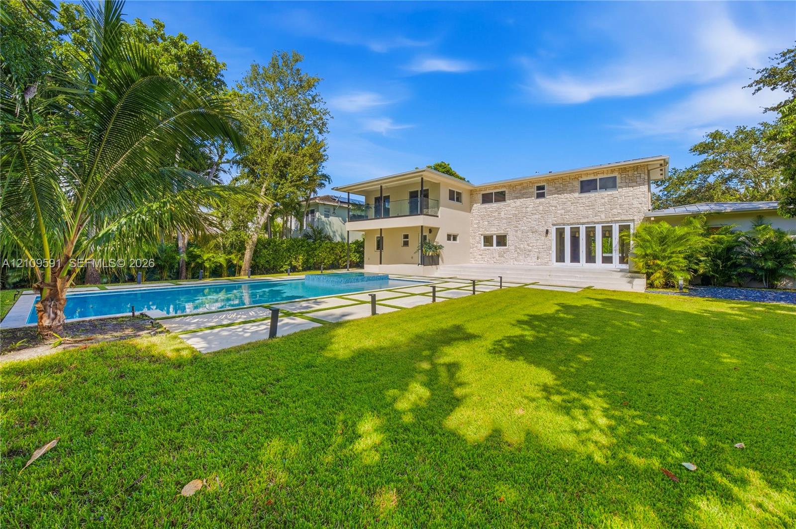Exterior facade featuring natural stone veneer, in-ground swimming pool with integrated spa, manicured lawn, tiered patio, and second-story balcony with glass railing
