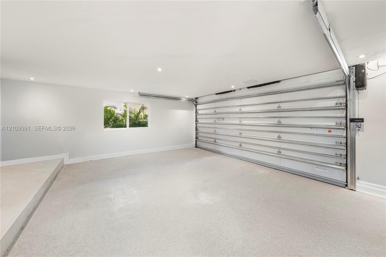 Garage interior featuring a seamless epoxy floor finish, recessed ceiling lighting, a white sectional garage door, and a single-pane window
