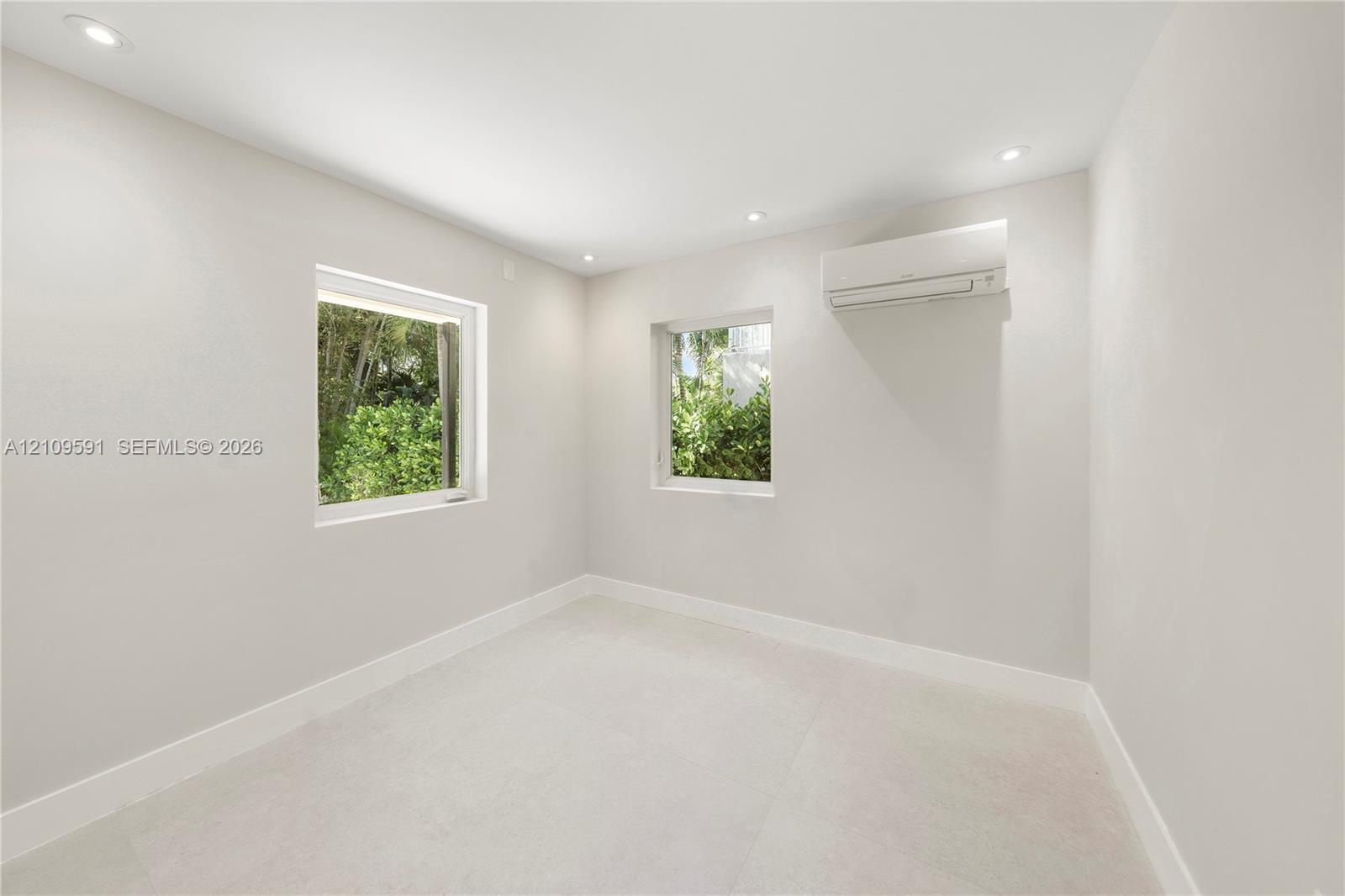Neutral interior space featuring recessed ceiling lighting, light-toned flooring, two windows, and a wall-mounted ductless air conditioning unit