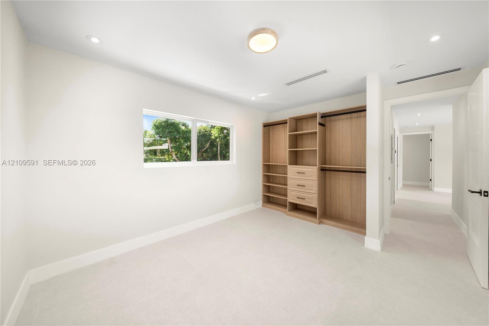 Room featuring neutral wall-to-wall carpeting, recessed ceiling lighting, a rectangular window, and custom built-in cabinetry with integrated shelving and drawers