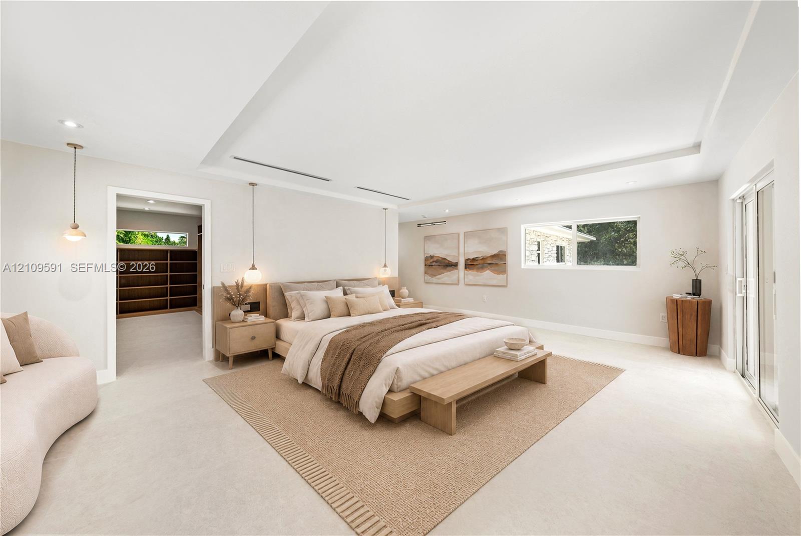 Virtually Staged: Spacious room with recessed tray ceiling, neutral stone-finish flooring, built-in shelving, pendant lighting, and sliding glass doors