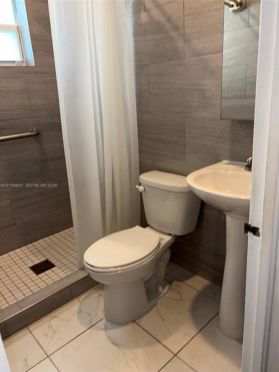 Full-height horizontal tile wall finishes, walk-in shower with square mosaic flooring, pedestal sink, and large-format porcelain tile flooring