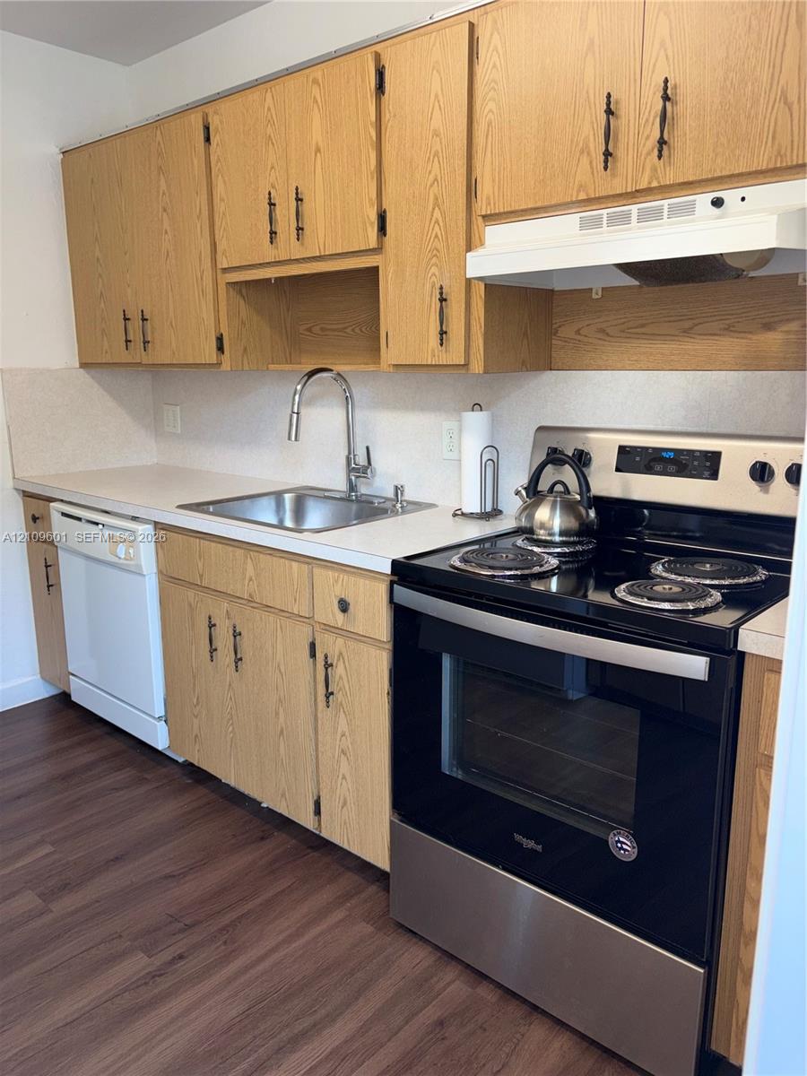 Kitchen featuring wood cabinetry with matte black pulls, stainless steel sink with high-arc pull-down faucet, white solid-surface countertops, wood-finish flooring, and a stainless steel electric range