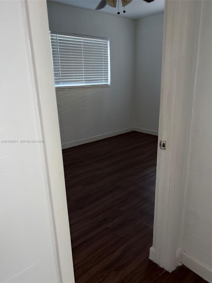 Room featuring dark wood-finish flooring, white walls, horizontal window blinds, and a ceiling fan