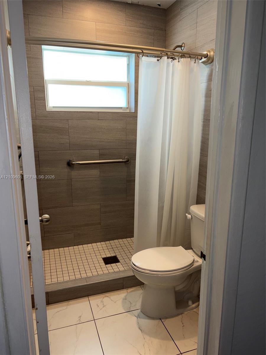Full-height wall tiling in wood-finish ceramic, walk-in shower with mosaic tile flooring, horizontal transom window, and white large-format floor tiling