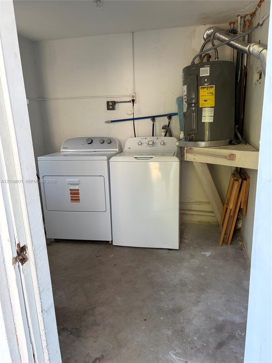 Dedicated utility/laundry space featuring a concrete floor, built-in shelving, and an electric water heater & a Full Sized Washer & Dryer.