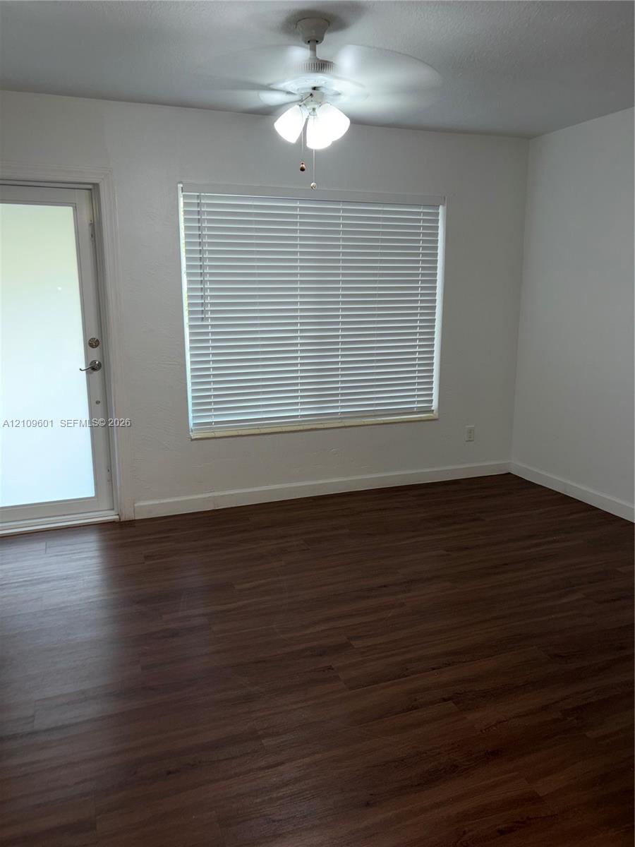 Wood-finish flooring, white walls, ceiling fan with light fixture, window with horizontal blinds, and glass-paneled exterior door