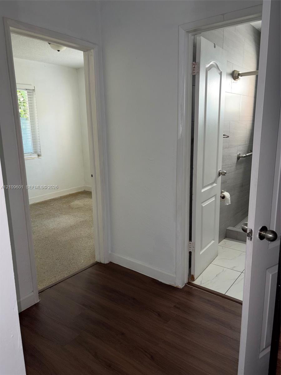 Interior hallway featuring wood-finish flooring, two-panel interior doors, and a bathroom with large-format wall tile and stone-finish floor tile