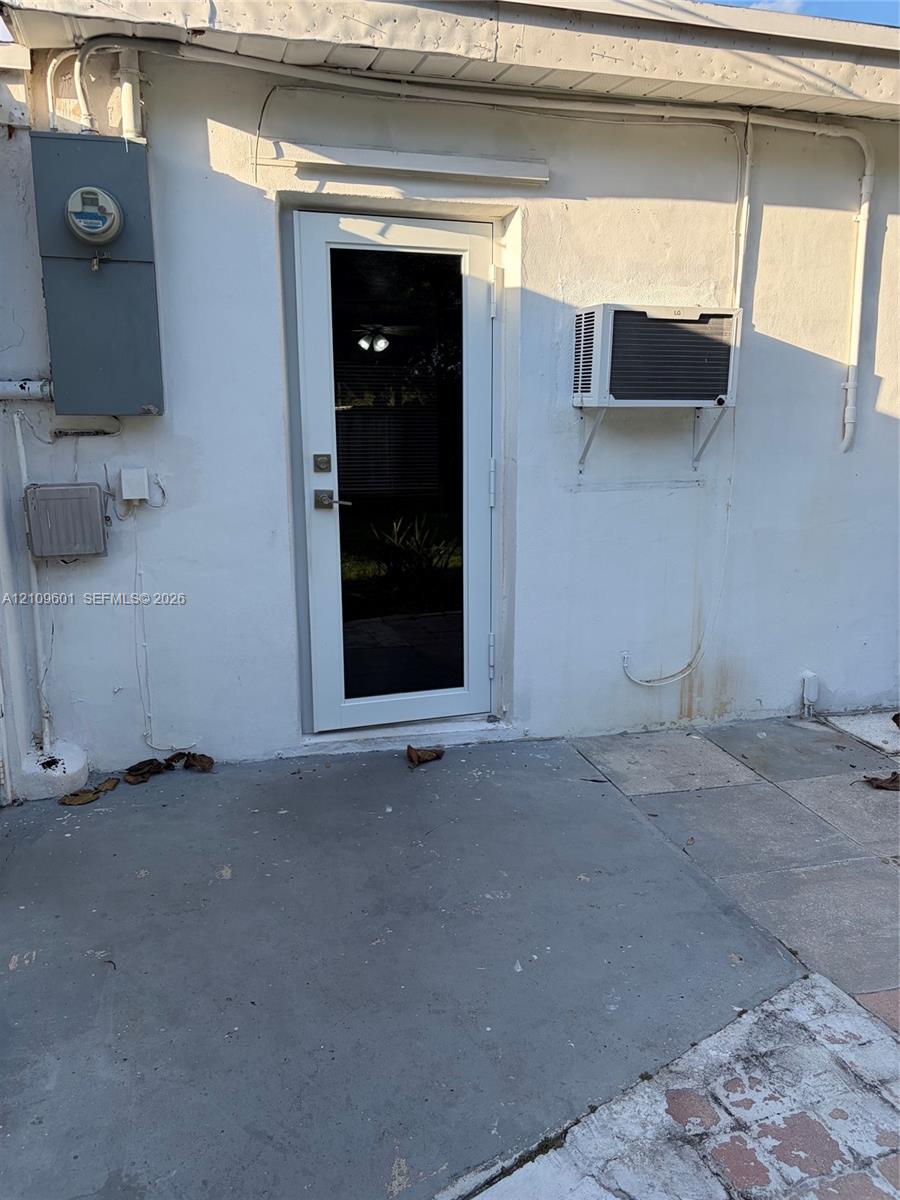 Exterior entry featuring a glass-panel door, concrete patio surface, and a wall-mounted cooling unit
