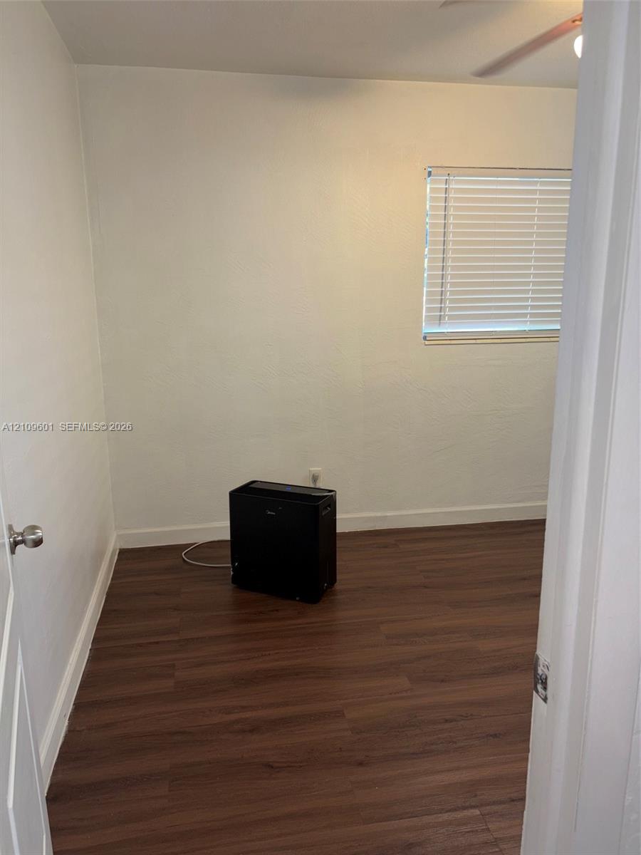 Room featuring wood-finish flooring, smooth white walls, and a window fitted with horizontal blinds