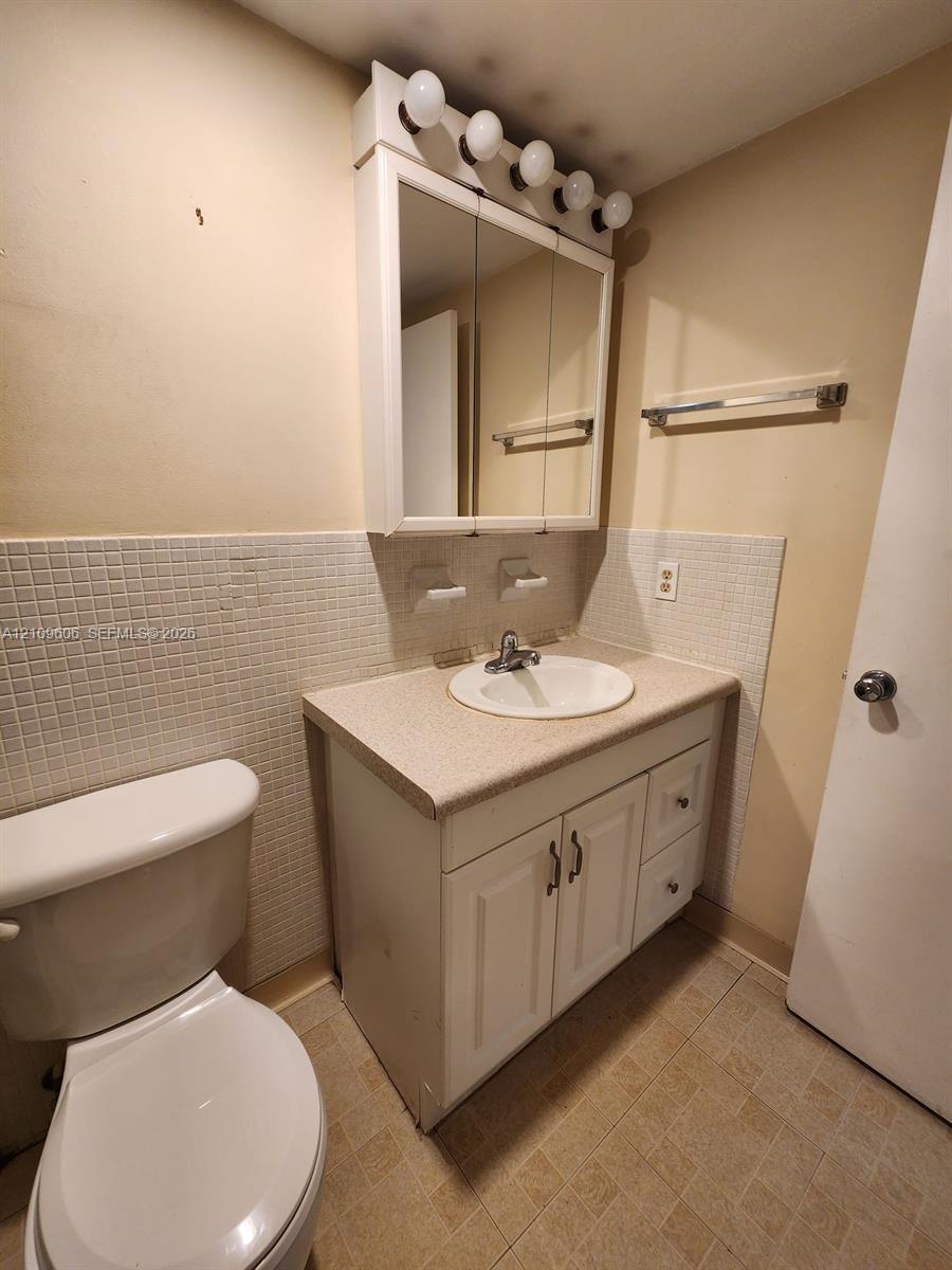 Bathroom vanity featuring a solid-surface countertop, integrated basin, white cabinetry with storage drawers, tri-view medicine cabinet with integrated light fixture, and tiled backsplash