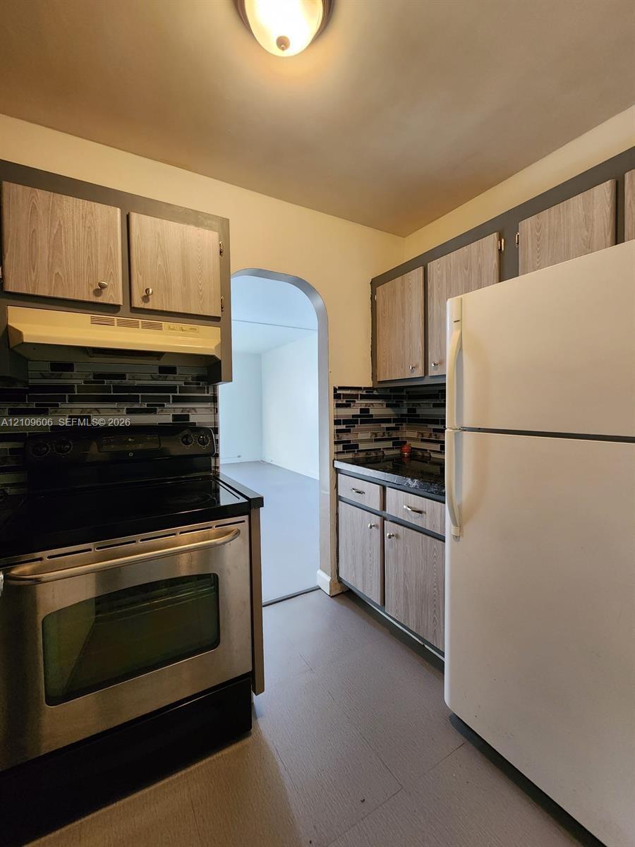 Kitchen featuring wood-finish cabinetry, a stainless steel range, a dark linear-tile backsplash, and an arched doorway