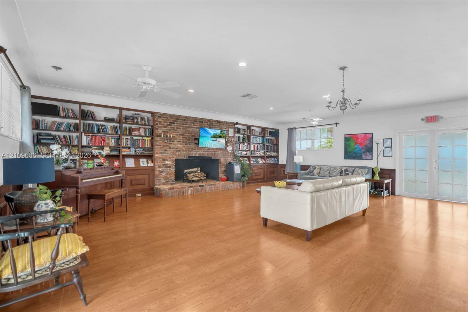 Expansive room featuring wood-finish flooring, floor-to-ceiling wood bookshelves, a brick fireplace with a raised hearth, and double French doors