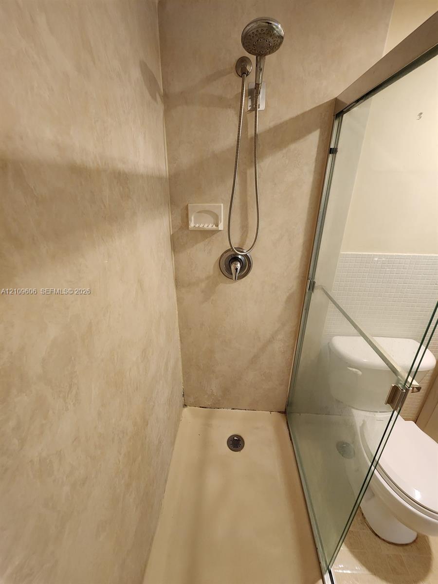 Walk-in shower enclosure with beige wall surround, integrated soap niche, handheld showerhead fixture, and glass door panel