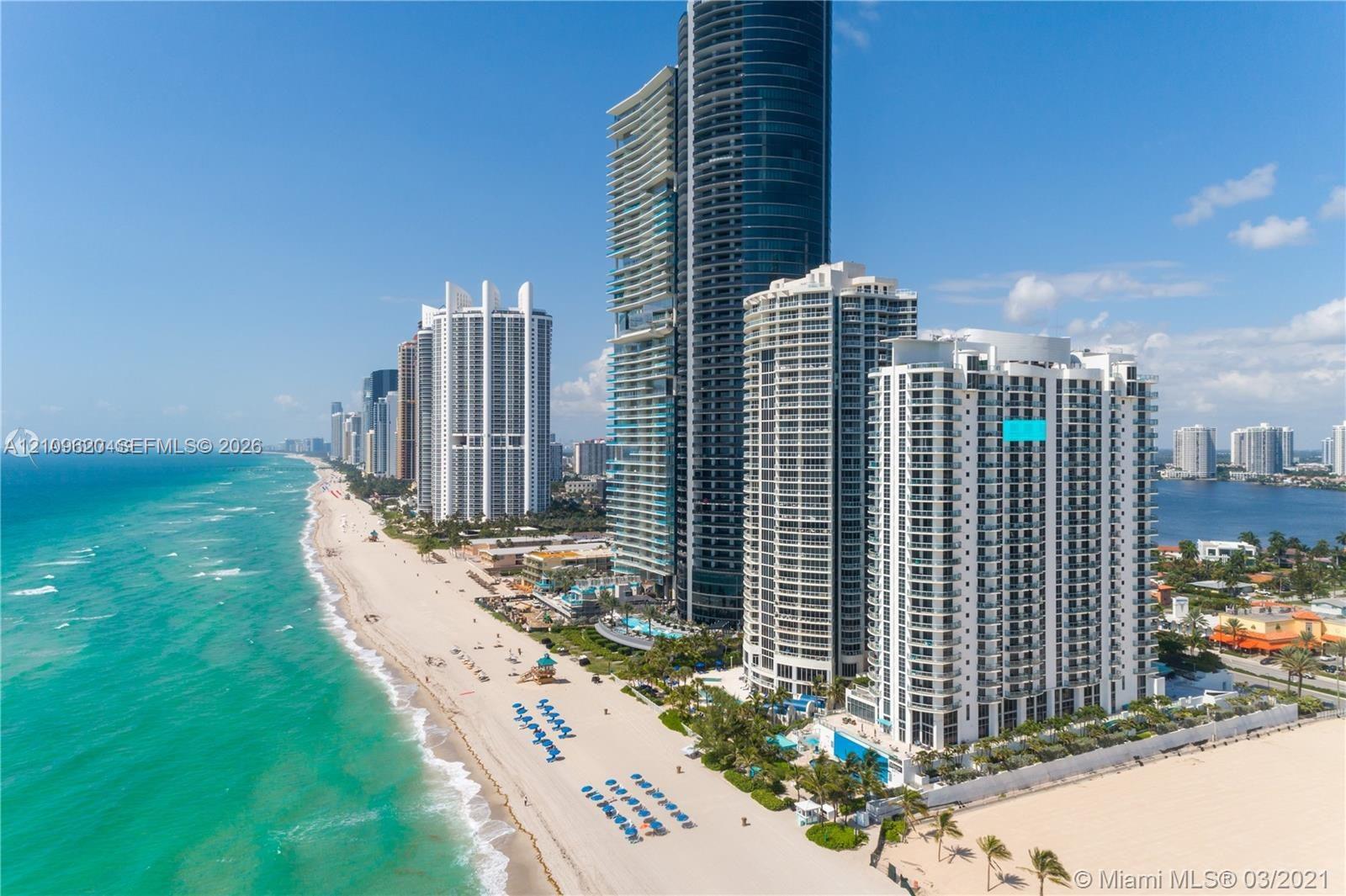 High-rise residential building featuring expansive glass balconies, direct beachfront positioning, and exterior swimming pool area