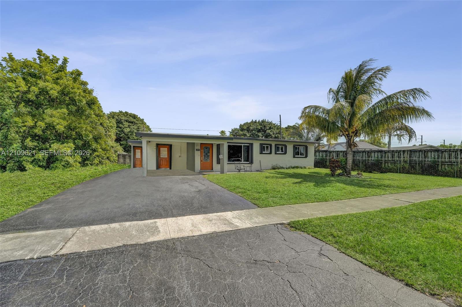 Single-story exterior featuring a flat roofline, paved driveway, covered entryway, and mature palm tree