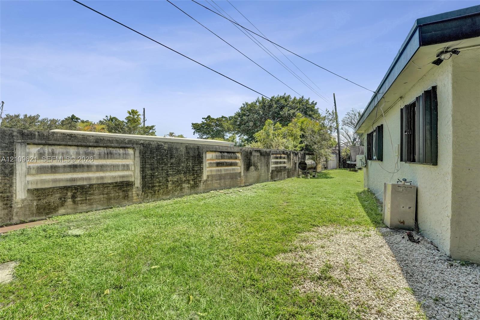Side yard featuring a grass lawn, decorative concrete block perimeter wall, and gravel ground cover