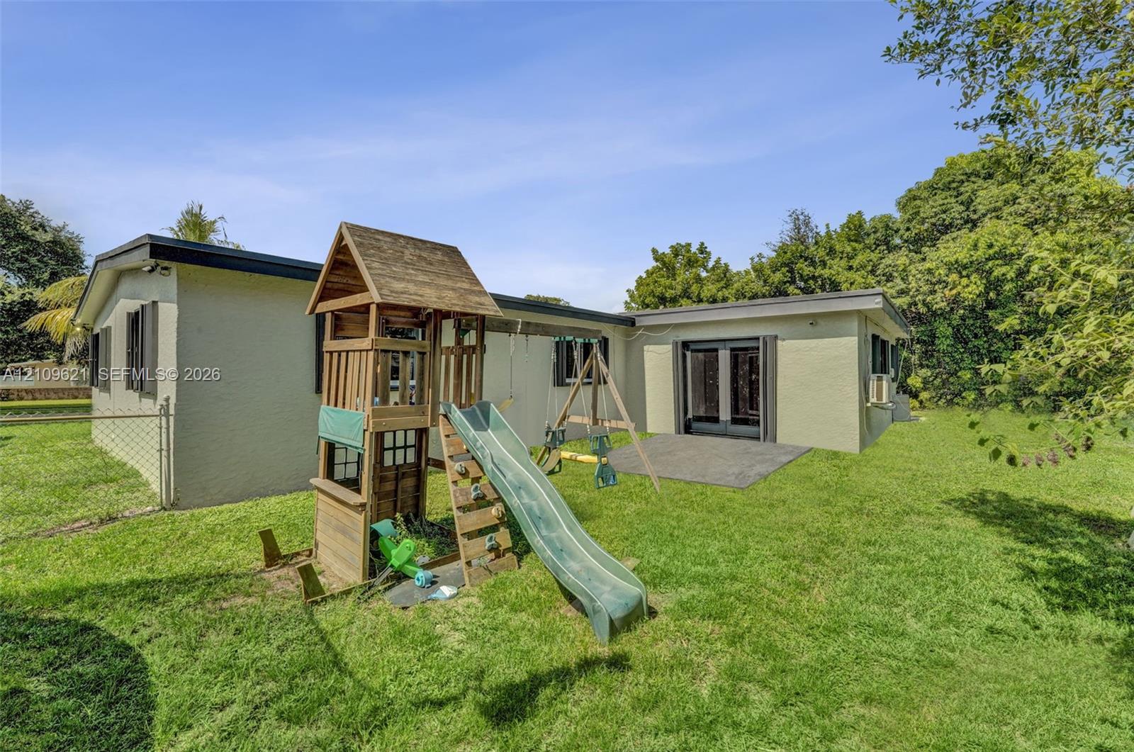 Fenced backyard featuring a paved patio, exterior double doors, and established greenery