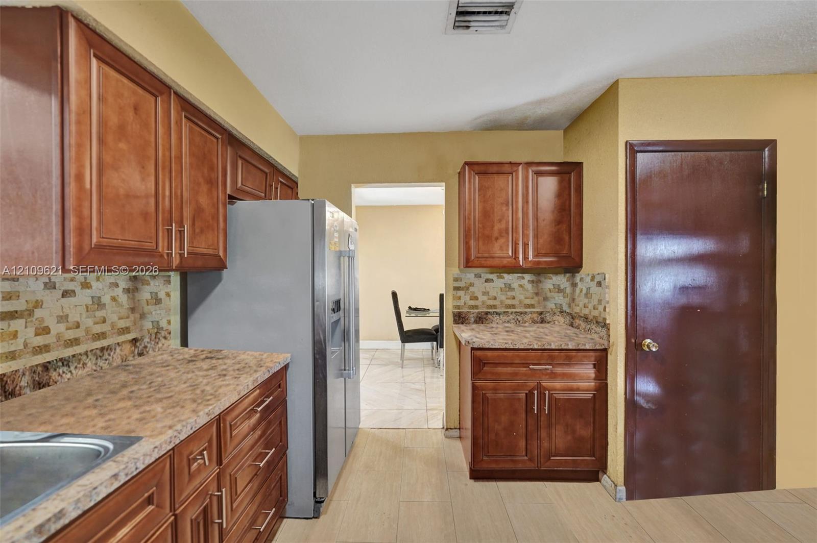 Kitchen featuring wood-finish cabinetry, stone-patterned laminate countertops, and a textured tile backsplash