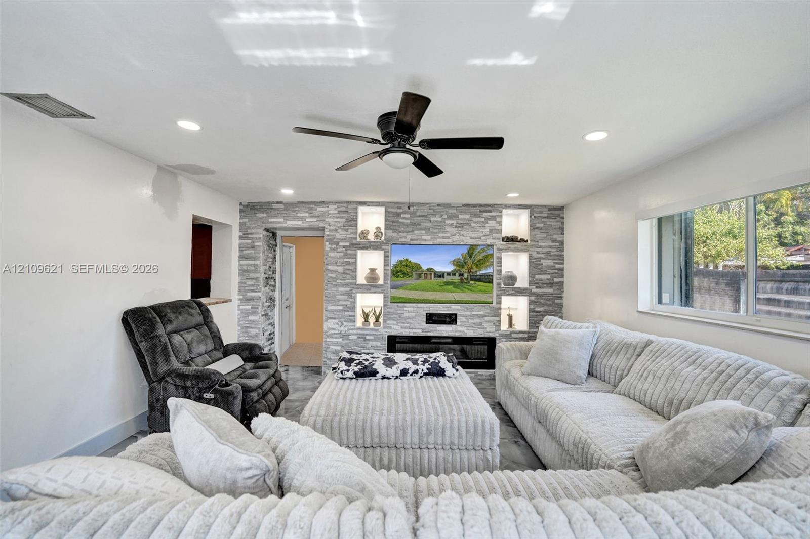 Living area featuring a floor-to-ceiling stacked stone accent wall with integrated recessed shelving and a built-in electric fireplace, recessed lighting, and a ceiling fan