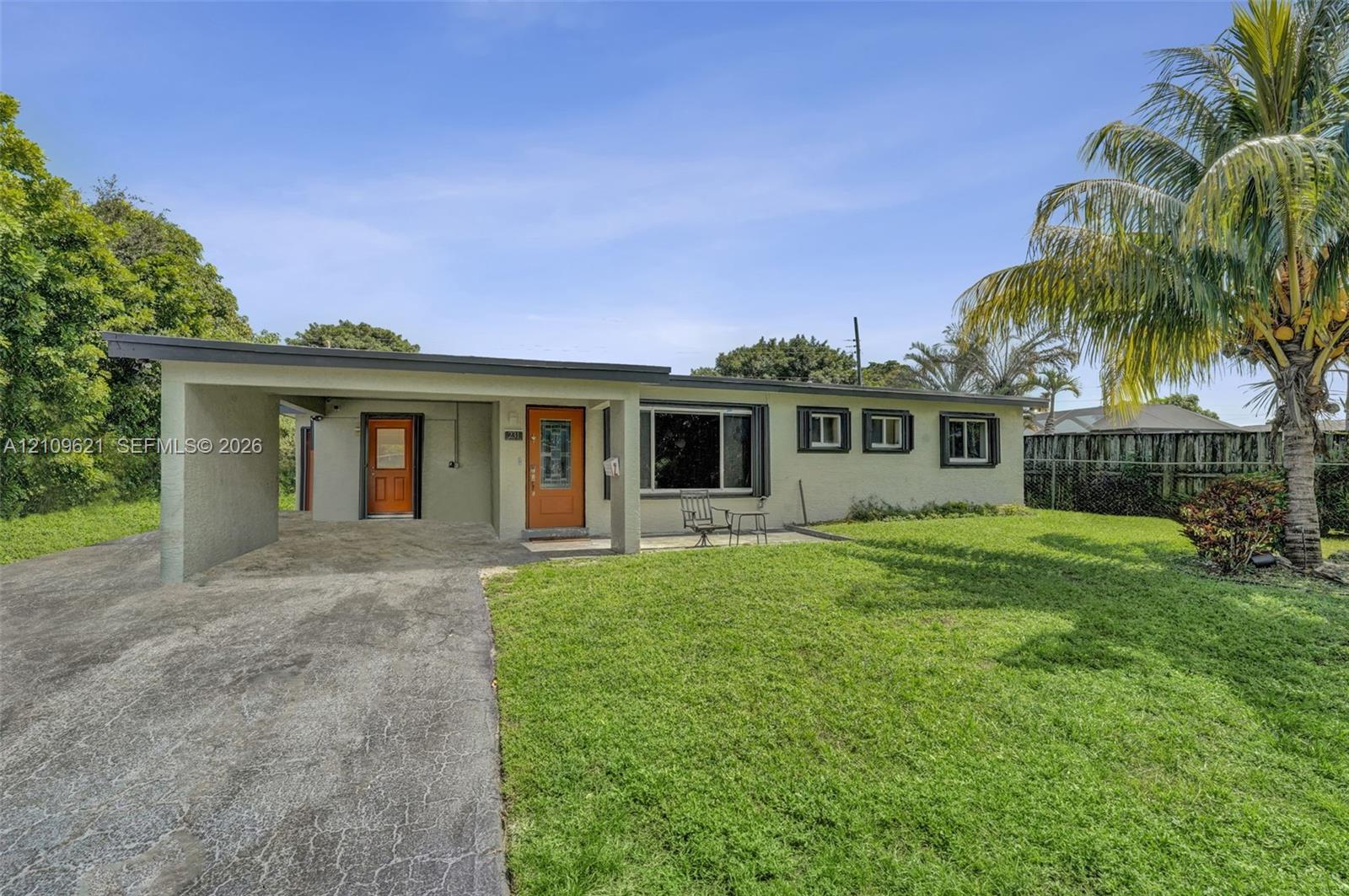 Single-story exterior featuring a flat roofline, attached carport, concrete driveway, and front lawn with mature palm tree
