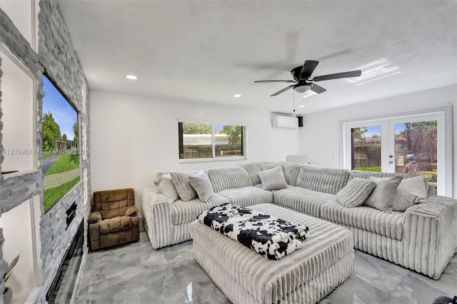 Floor-to-ceiling stone-textured accent wall with integrated shelving, built-in electric fireplace, recessed lighting, ceiling fan, and large-format tile flooring