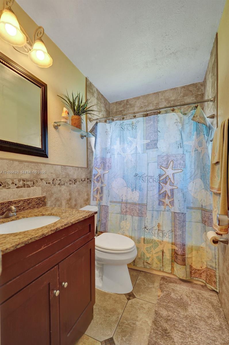 Bathroom featuring a vanity with stone-finish countertop, integrated sink, wall-mounted lighting, tile flooring, and a tile-surround tub enclosure
