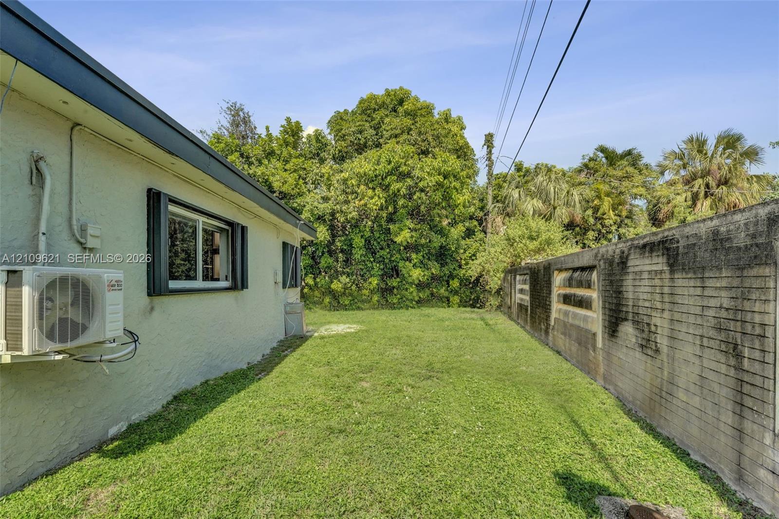 Side yard featuring a manicured lawn, masonry perimeter wall, and mature tree landscaping