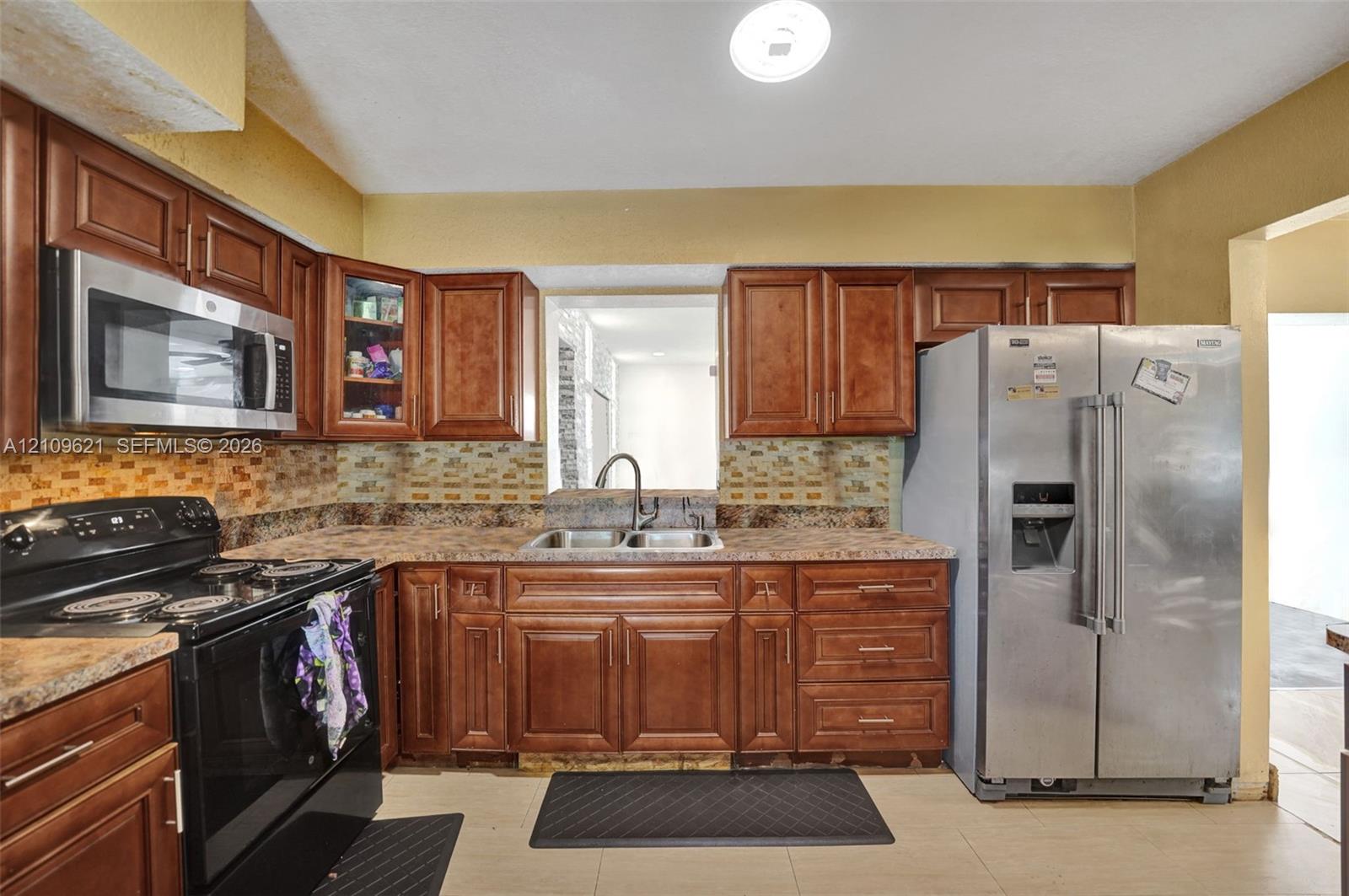 Kitchen featuring stained-wood cabinetry, stone-finish countertops, stainless steel appliances, a mosaic tile backsplash, and a dual-basin sink with a gooseneck faucet