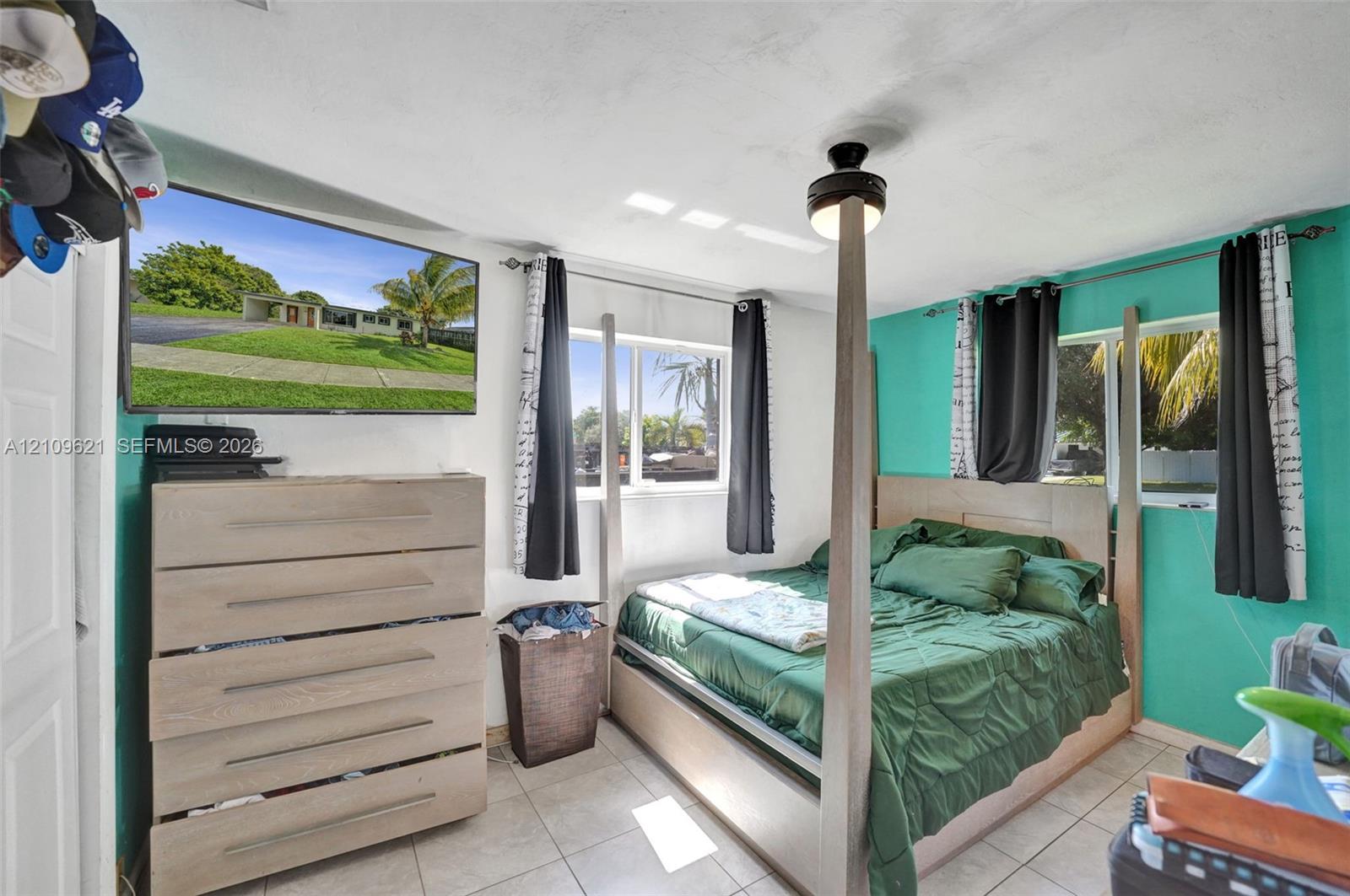 Bedroom featuring tile flooring, dual-aspect windows, and a ceiling fan with integrated lighting